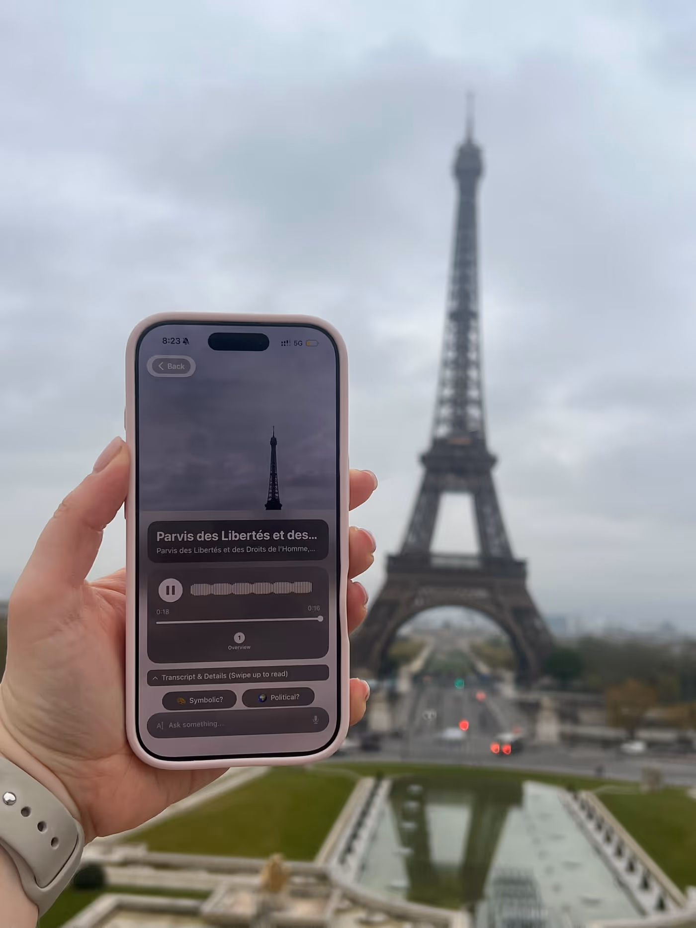A hand holds an iPhone running Chiaro; on screen it recognizes the Eiffel Tower, which rises in the background.